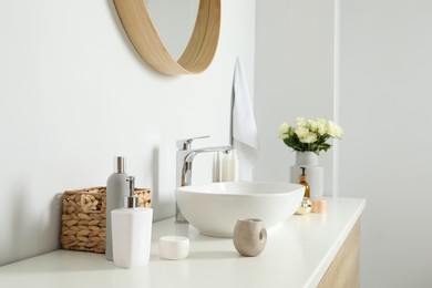 Photo of Vase with beautiful white roses and toiletries near sink in bathroom