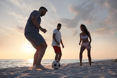 Friends playing football on beach at sunset