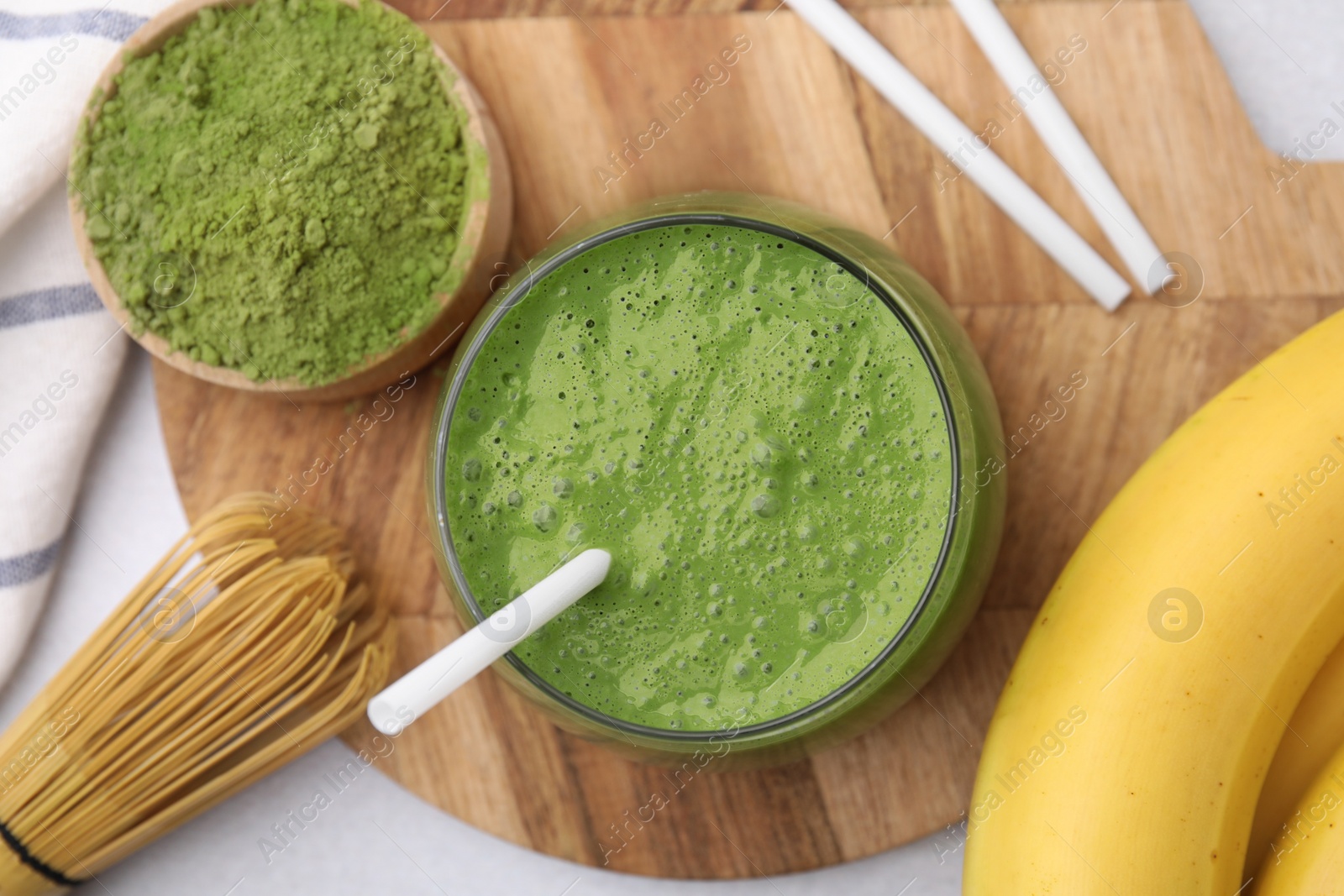 Photo of Glass of tasty matcha smoothie, powder, bamboo whisk and banana on light table, flat lay