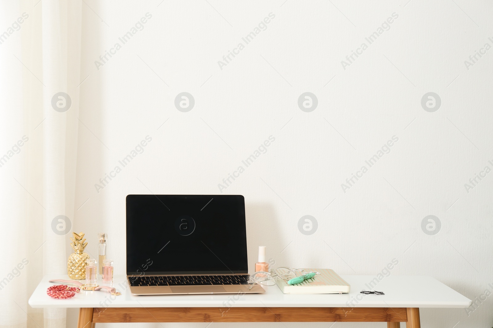 Photo of Stylish workplace with modern laptop and cosmetic products on table near light wall, space for text. Beauty blogger