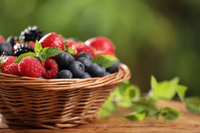 Photo of Wicker bowl with different fresh ripe berries and mint on wooden table outdoors, space for text