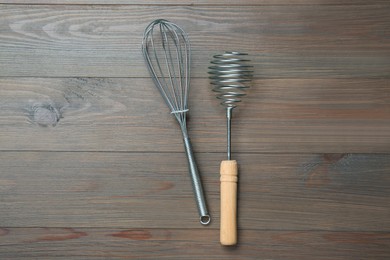 Two metal whisks on wooden table, top view