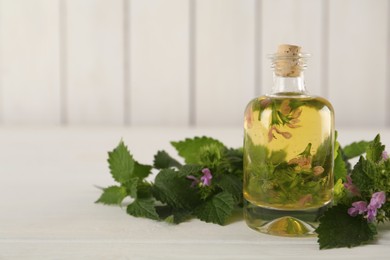 Photo of Glass bottle of nettle oil with flowers and leaves on white wooden table, closeup. Space for text