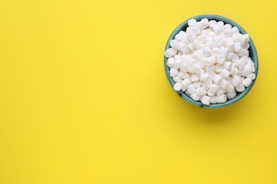 Photo of Bowl with delicious marshmallows on yellow background, top view. Space for text