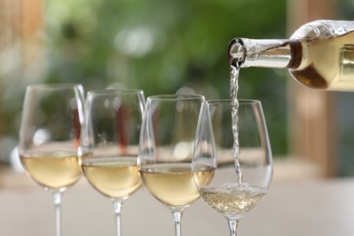 Photo of Pouring white wine from bottle into glass on blurred background