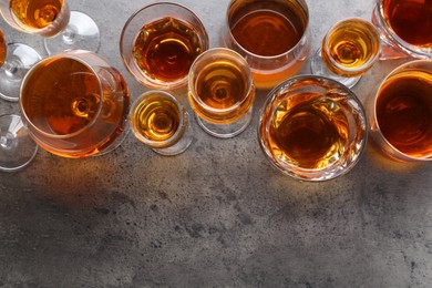 Photo of Different delicious liqueurs in glasses on grey table, flat lay. Space for text