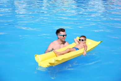 Little boy on inflatable mattress with father in swimming pool