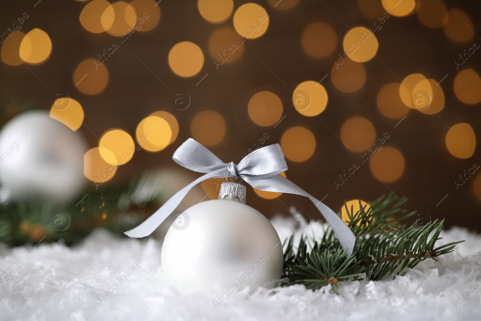 Photo of Beautiful Christmas ball and fir branch on snow against blurred festive lights. Space for text