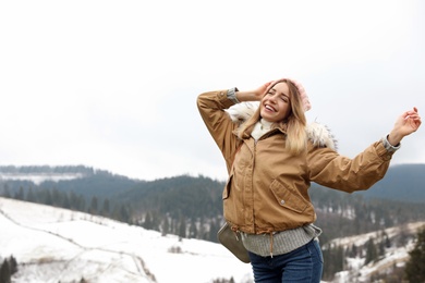 Young woman in warm clothes near snowy hill, space for text. Winter vacation