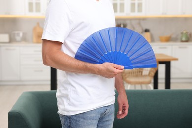 Photo of Man with blue hand fan in kitchen, closeup