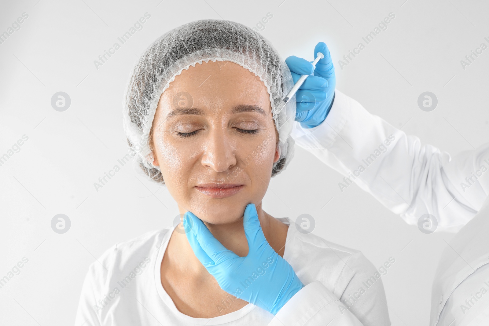 Photo of Mature woman getting facial injection on white background. Cosmetic surgery concept