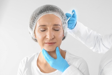 Mature woman getting facial injection on white background. Cosmetic surgery concept