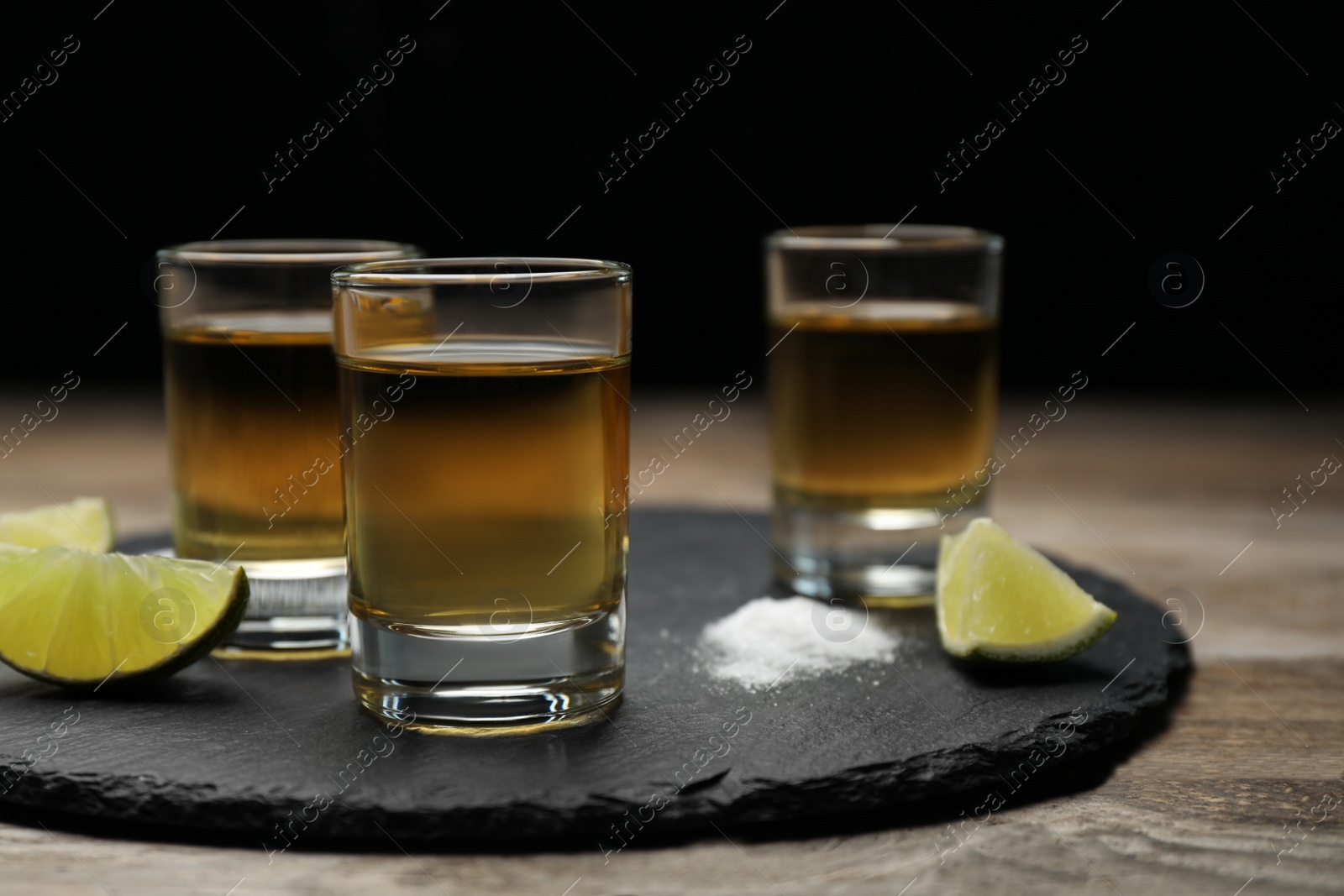 Photo of Mexican Tequila shots, lime slices and salt on wooden table