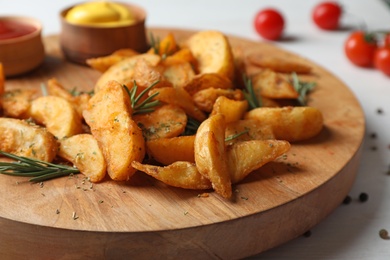 Photo of Wooden board with baked potatoes and rosemary on table, closeup