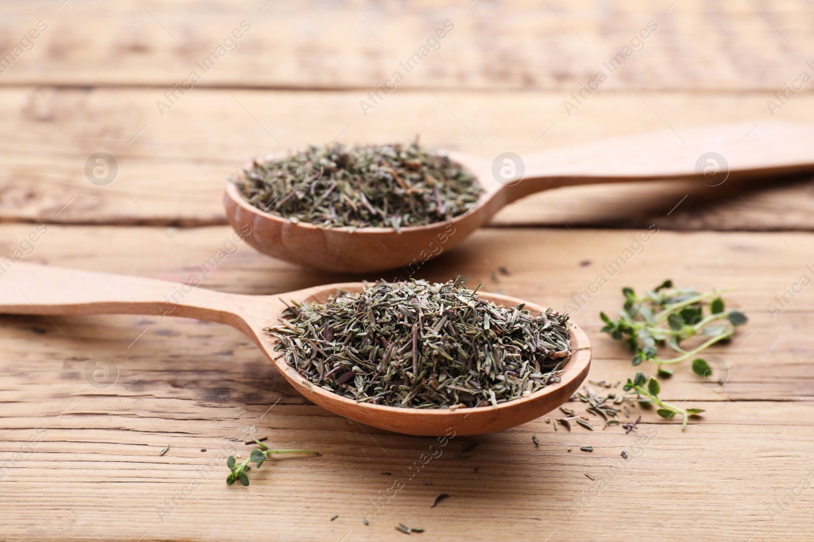 Photo of Spoons with dried and fresh thyme on wooden table, closeup