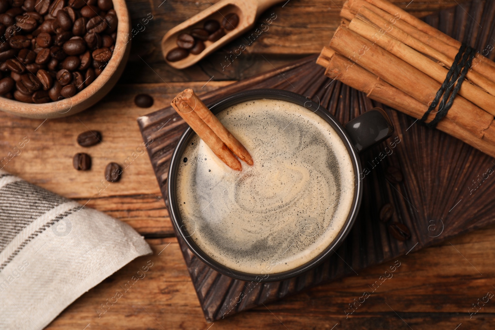 Photo of Cup of hot coffee with aromatic cinnamon on wooden table, flat lay