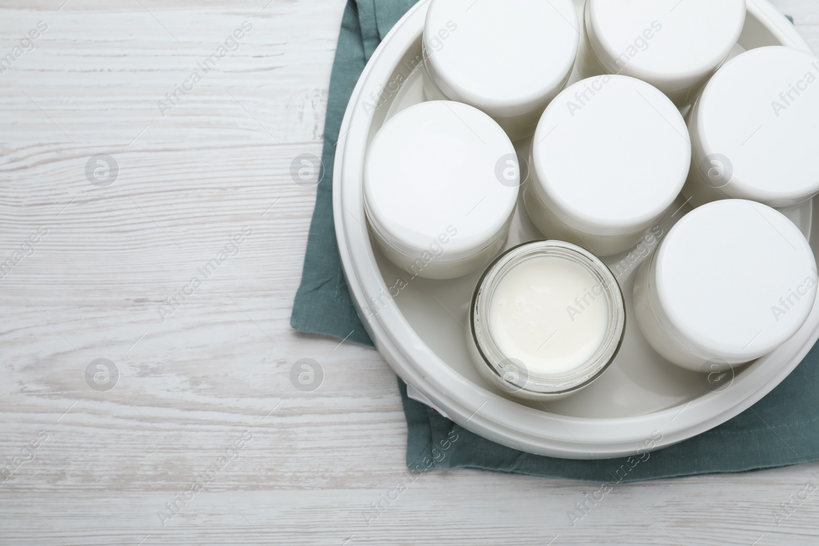 Photo of Modern yogurt maker with full jars on white wooden table, top view. Space for text