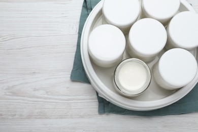 Photo of Modern yogurt maker with full jars on white wooden table, top view. Space for text