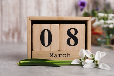 Photo of Women's day greeting card. Block calendar and beautiful snowdrops on grey table