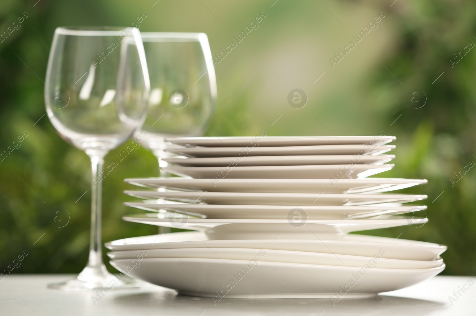 Photo of Set of clean dishware and wineglasses on grey table against blurred background