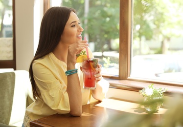 Photo of Young woman with glass of tasty natural lemonade in cafe. Detox drink
