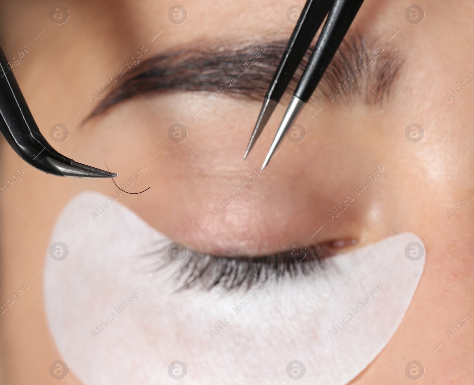 Photo of Young woman undergoing eyelashes extensions procedure, closeup