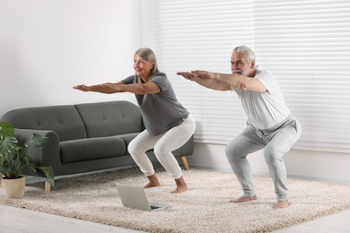 Senior couple practicing yoga with laptop on carpet at home