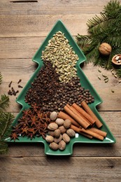 Different spices, nuts and fir branches on wooden table, flat lay