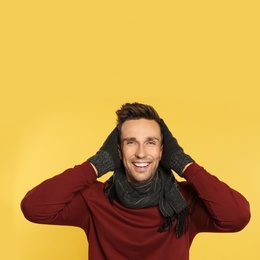 Photo of Happy young man in warm clothes on yellow background. Winter season