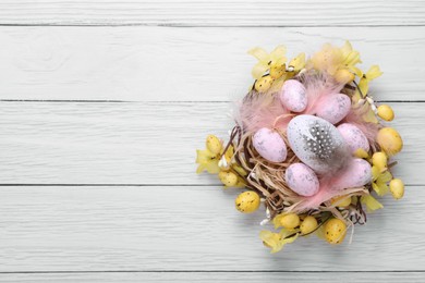 Photo of Festively decorated Easter eggs on white wooden table, top view. Space for text