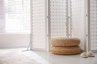 Stylish room interior with white folding screen and wicker poufs