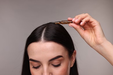 Photo of Beautiful young woman using ampoule for hair treatment on grey background, closeup