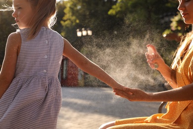 Photo of Mother applying insect repellent onto girl's hand outdoors, closeup