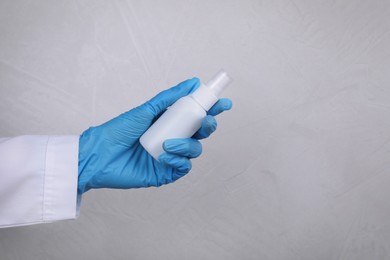 Doctor holding antiseptic on light grey background, closeup
