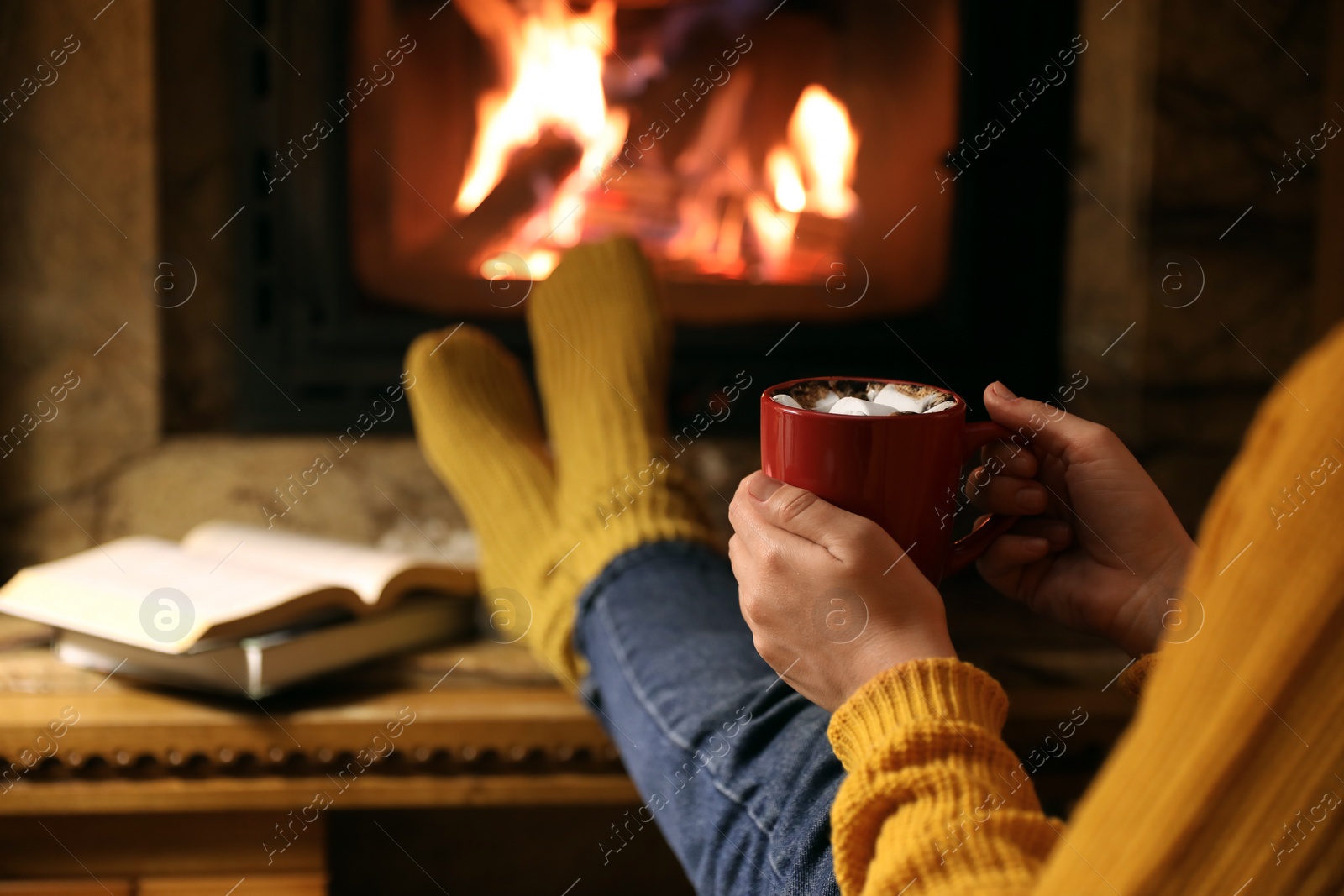 Photo of Woman with cup of hot drink resting near fireplace indoors, closeup. Space for text