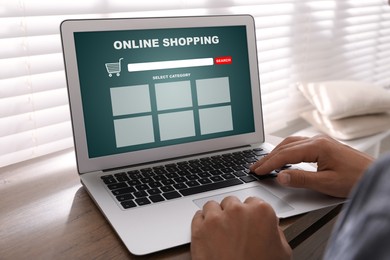 Image of Man using laptop for online shopping at wooden table, closeup