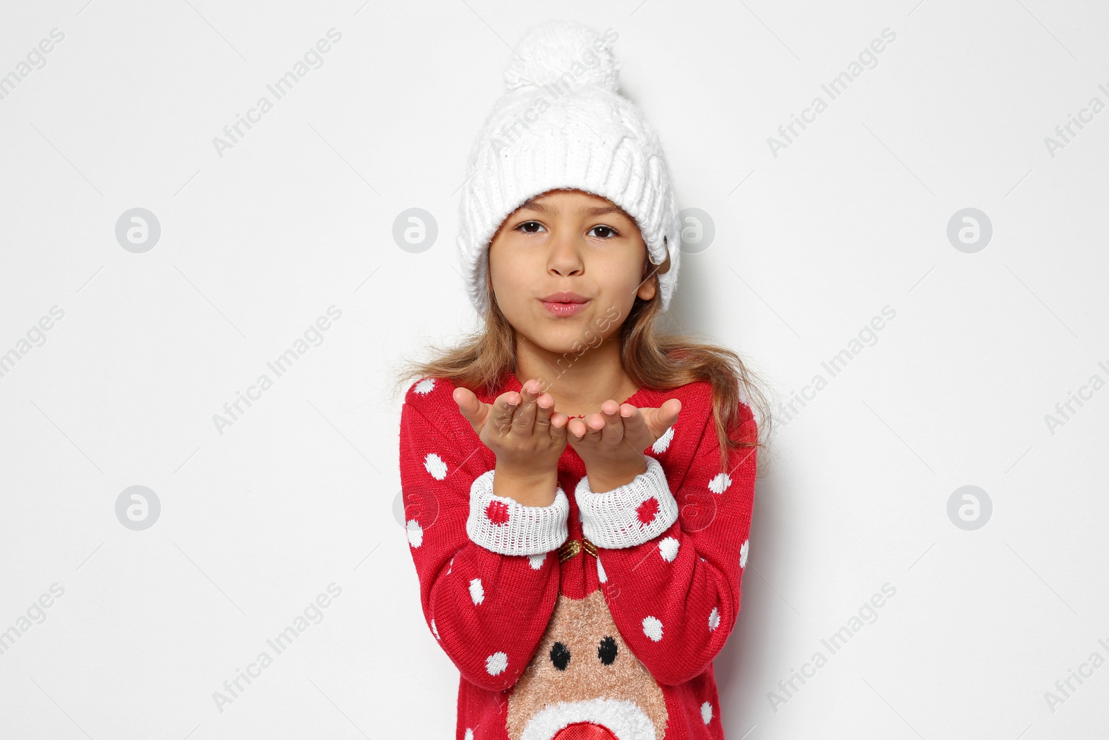 Photo of Cute little girl in Christmas sweater and knitted hat on white background