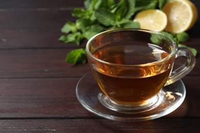 Photo of Glass cup of freshly brewed tea on wooden table, closeup. Space for text