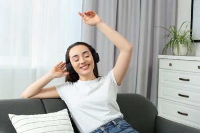 Photo of Happy woman in headphones enjoying music on soft sofa at home