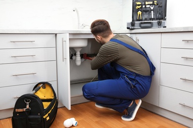 Photo of Male plumber in uniform repairing kitchen sink