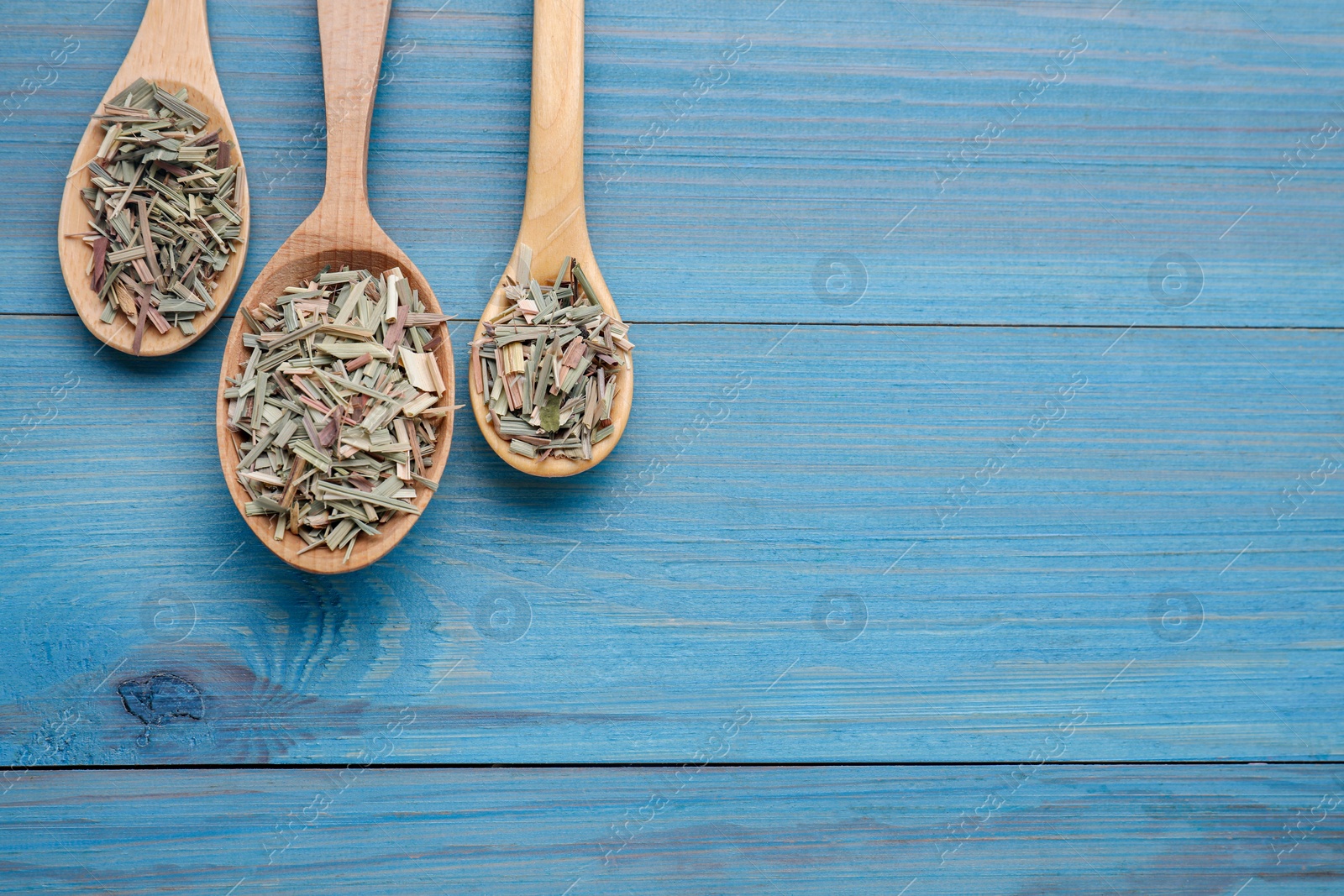 Photo of Spoons with aromatic dried lemongrass on light blue wooden table, flat lay. Space for text