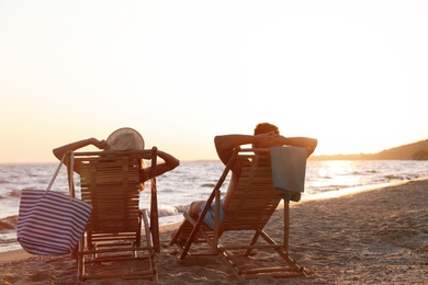 Young couple relaxing in deck chairs on beach near sea