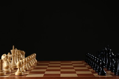 Chess pieces on wooden board against black background