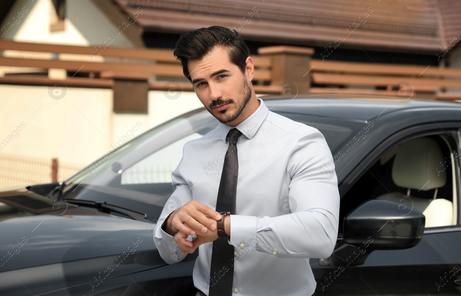 Photo of Attractive young man checking time near luxury car outdoors