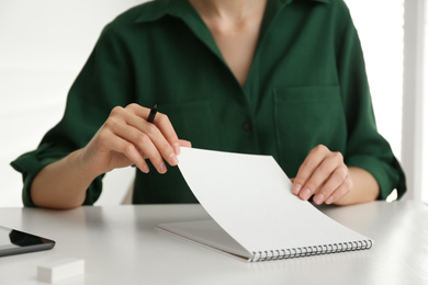 Photo of Woman with pencil and notepad at white table, closeup