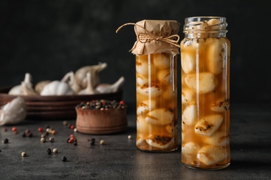 Photo of Preserved garlic in glass jars on table. Space for text