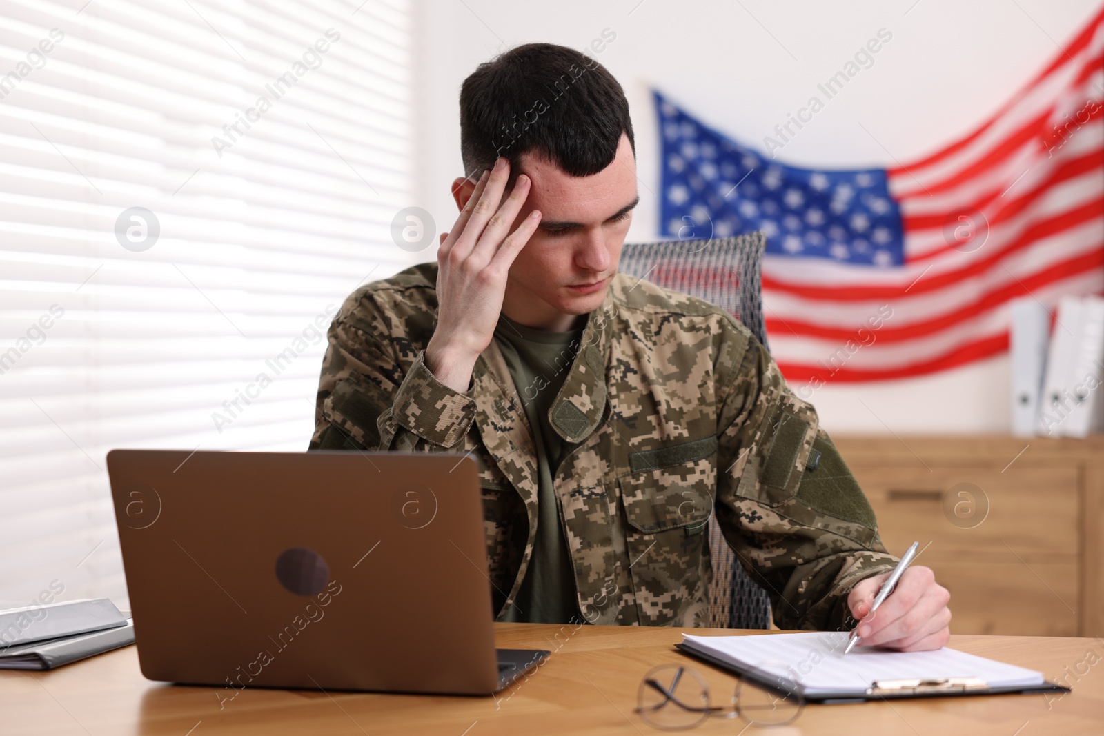 Photo of Military service. Young soldier working at table in office