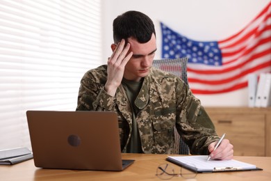 Photo of Military service. Young soldier working at table in office