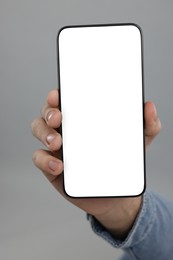 Man holding smartphone with blank screen on grey background, closeup