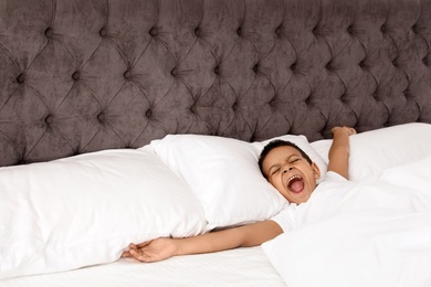 Photo of Cute little African-American boy yawning in bed. Sleeping time